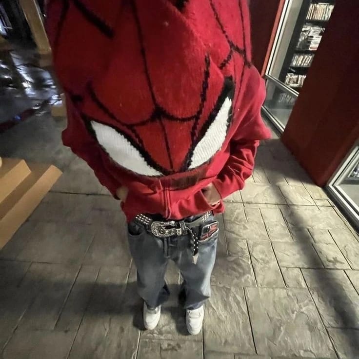 Person wearing a red hoodie with a spider design, standing indoors on a wooden floor.