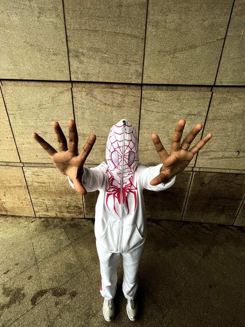 Person wearing a Spider-Man costume with a hood against a tiled wall.