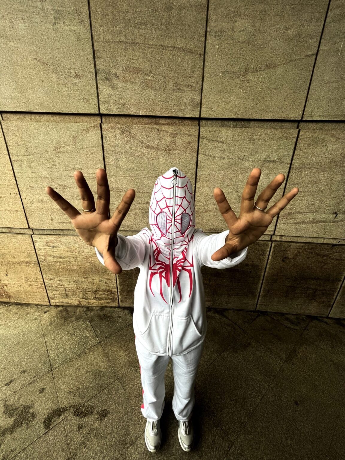Person wearing a Spider-Man costume with a hood against a tiled wall.